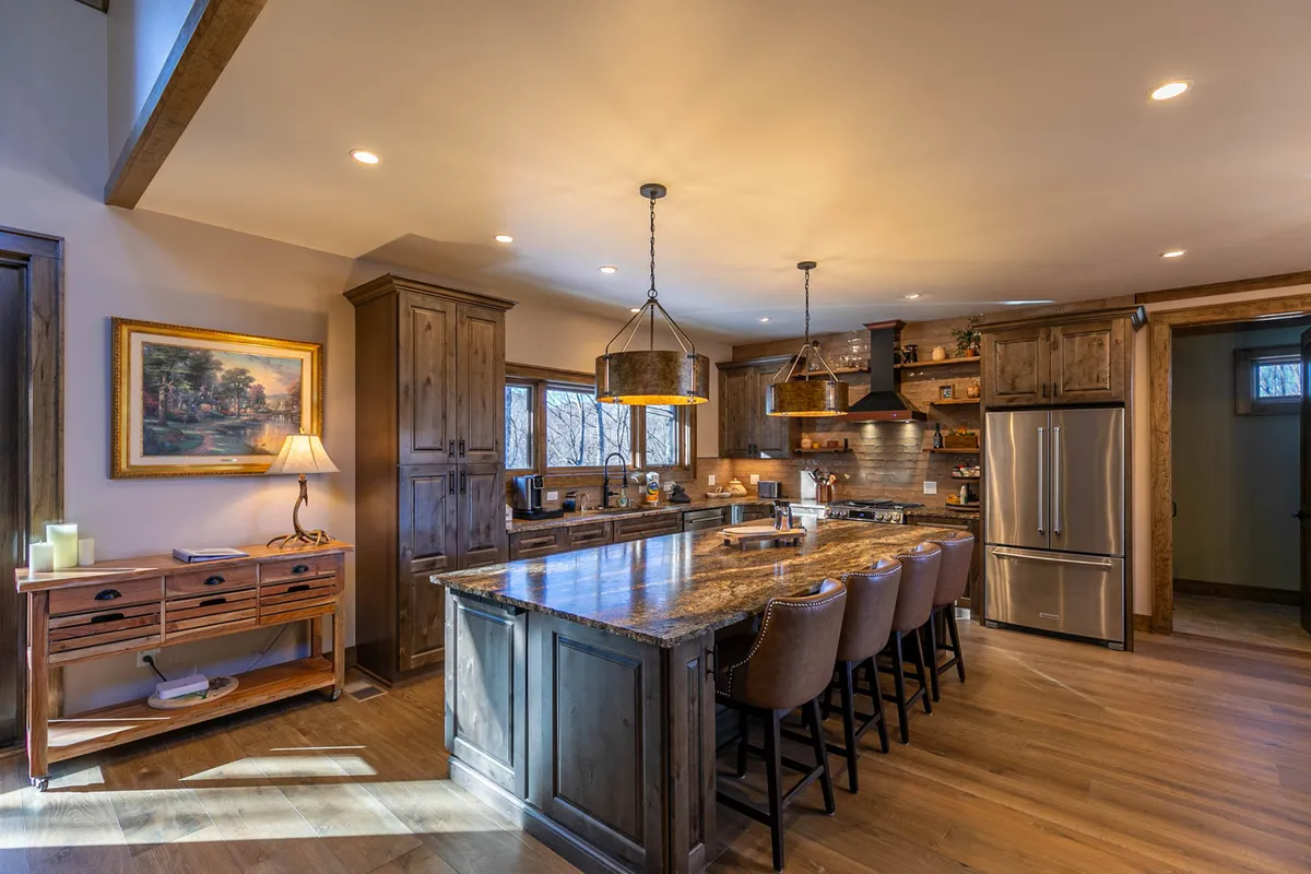 This image presents a spacious kitchen with a large granite island at its center, surrounded by warm wooden cabinetry and accented by stylish pendant lighting. The open layout showcases modern stainless steel appliances, ample counter space for meal preparation, and tasteful decorative touches that create an inviting, communal atmosphere.