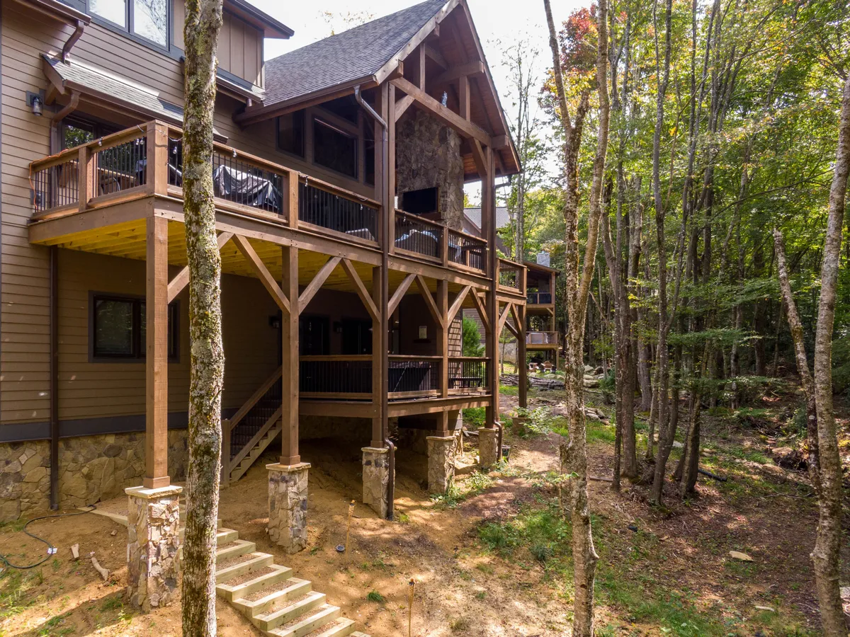 A handsome wooden deck with sturdy stone pillars is nestled among mature trees. This space is perfect for al fresco dining, morning coffee, or casual gatherings while soaking in the sights and sounds of the surrounding forest, further emphasizing the lodge’s immersion in nature.