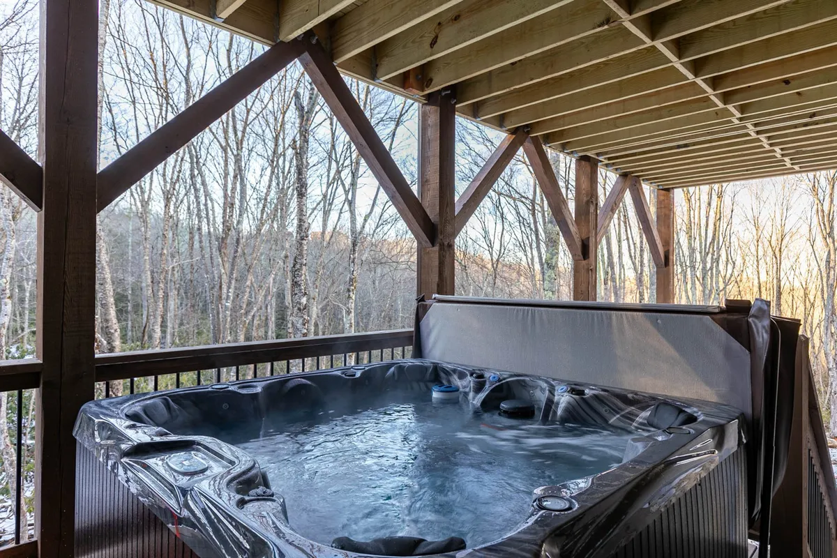 This image features a spacious hot tub set on a wooden deck, surrounded by tall trees and lush greenery, creating a tranquil, natural retreat. The setting exudes peace and relaxation, with the hot tub appearing inviting for groups or couples seeking to unwind while immersed in nature.