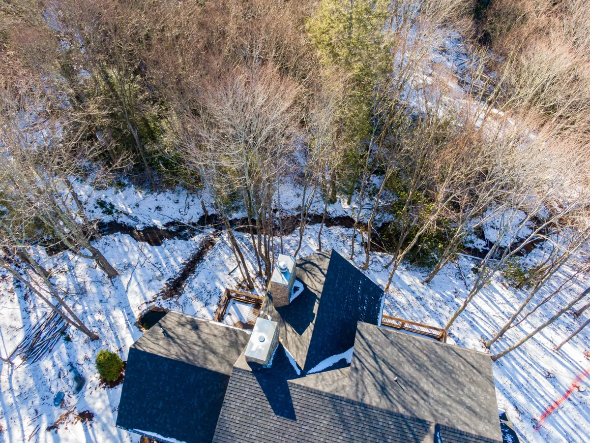 A wintry exterior view of a home’s roof surrounded by snow-laden trees and ground. The tranquil snowy landscape hints at winter activities and the peaceful retreat families can enjoy after days spent skiing at nearby resorts.