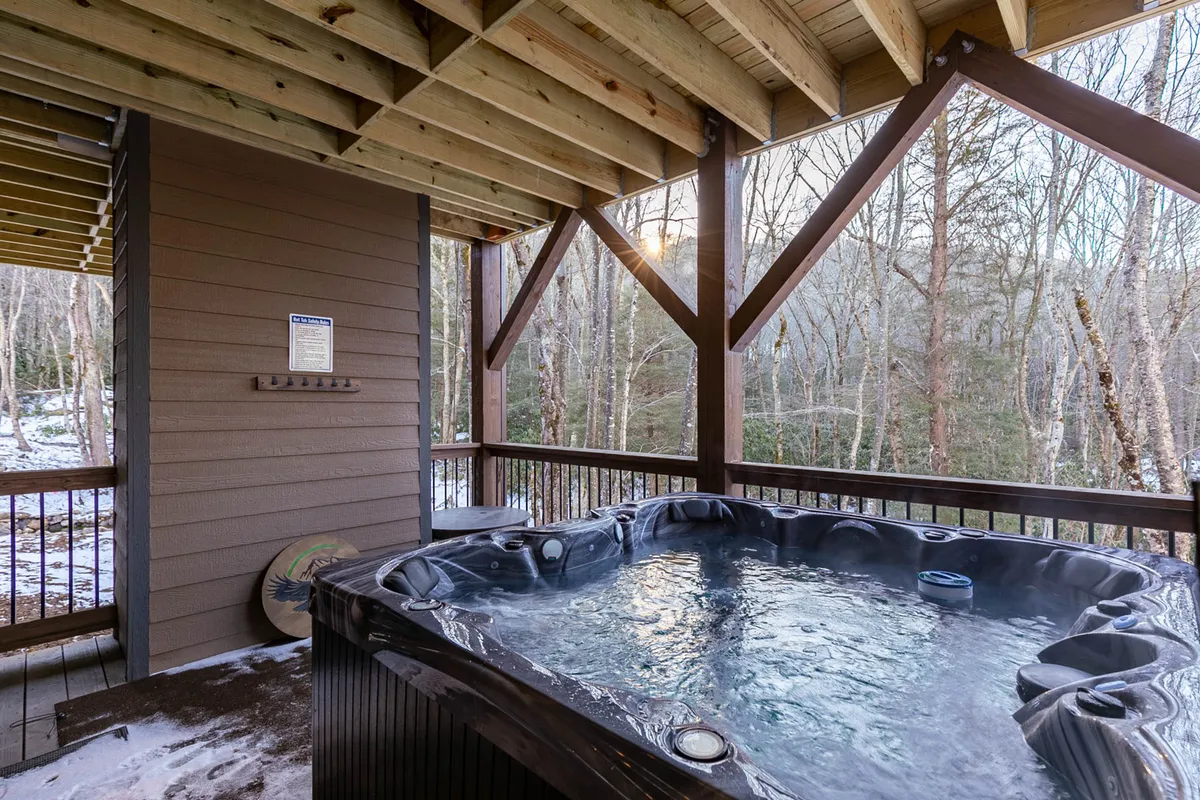 An inviting balcony scene with a private hot tub set against lush trees and a wooden structure, suggesting relaxation and seclusion. The setup evokes peaceful evenings soaking under the stars, enhanced by nature and ambient music.
