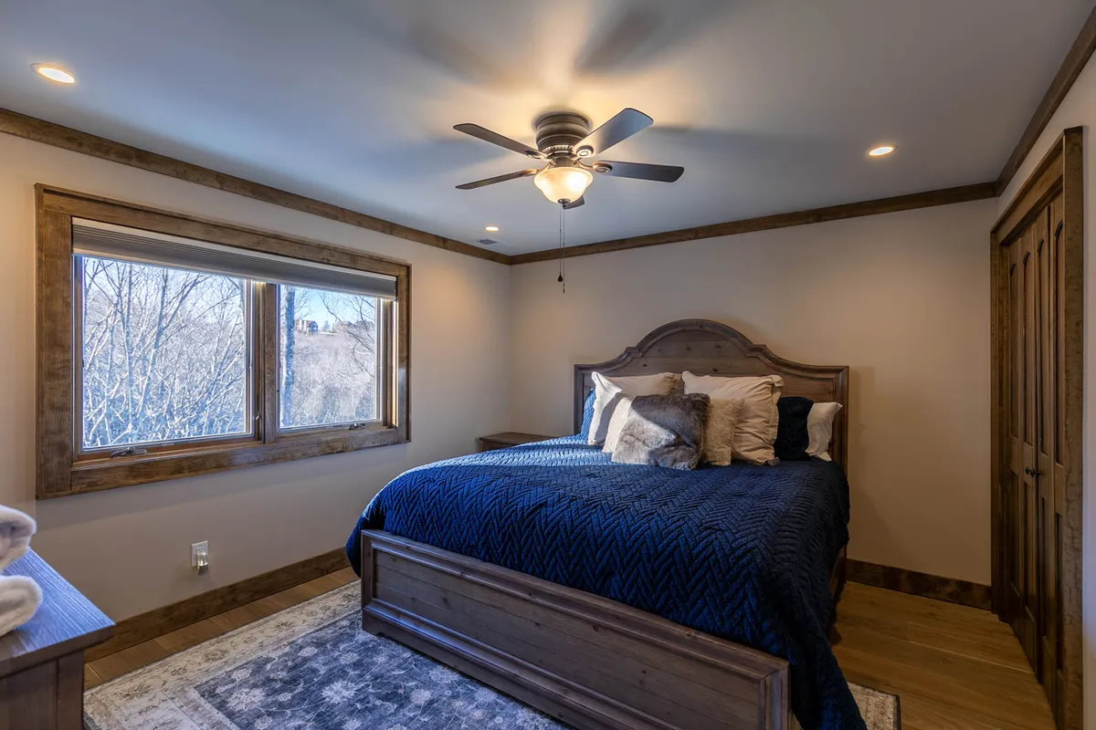 A tranquil bedroom with a soft, inviting bed, large windows letting in natural light, and a ceiling fan for comfort. The room evokes relaxation and restful mornings, with the outdoors visible through the windows, hinting at easy access to daily adventure.